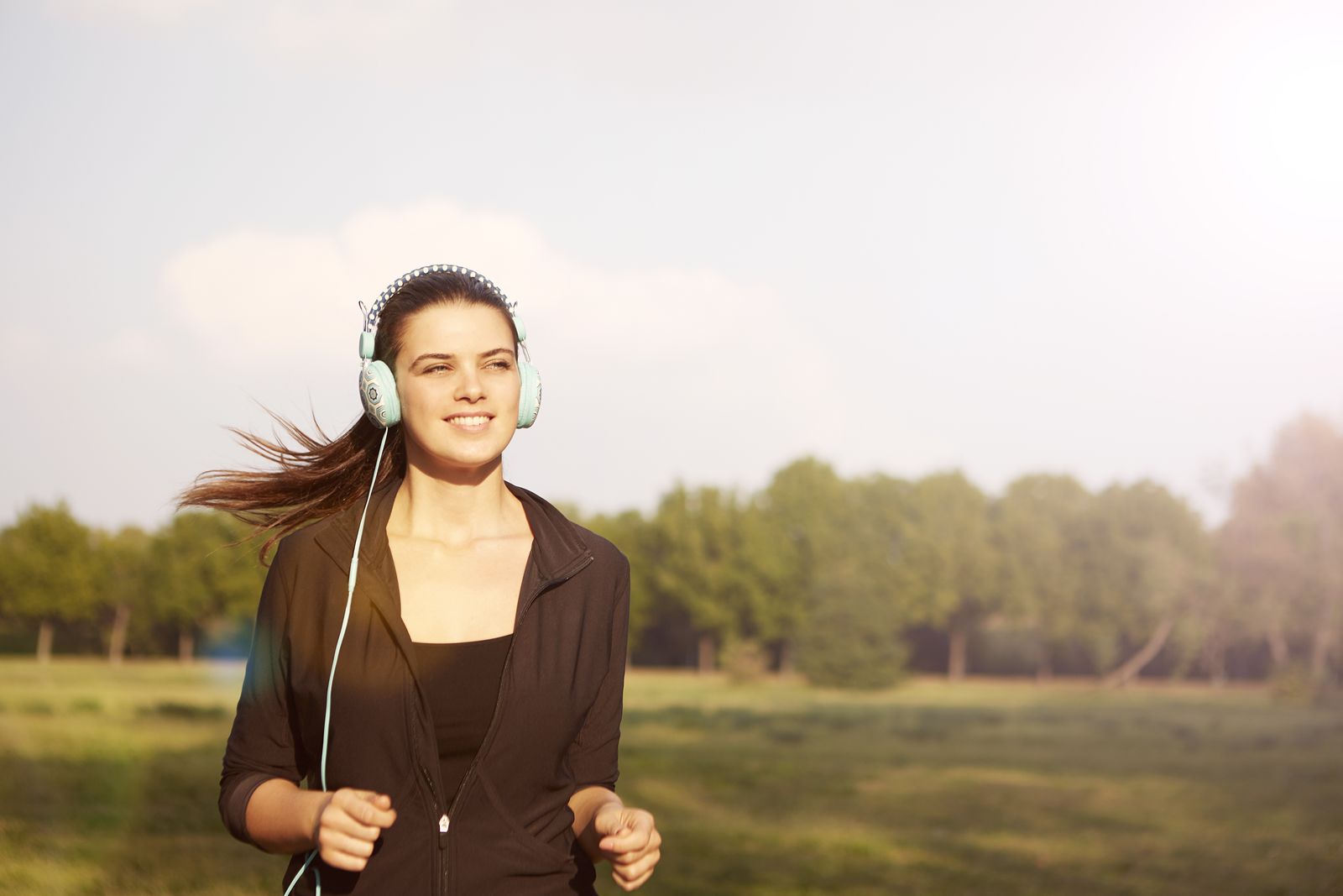 Young woman jogging through a sunlit field with headphones